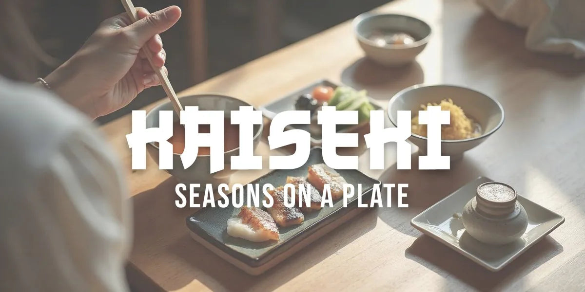 Hand with chopsticks reaches across a low table, multiple small ceramic dishes and soup bowls containing seasonal courses, soft natural light