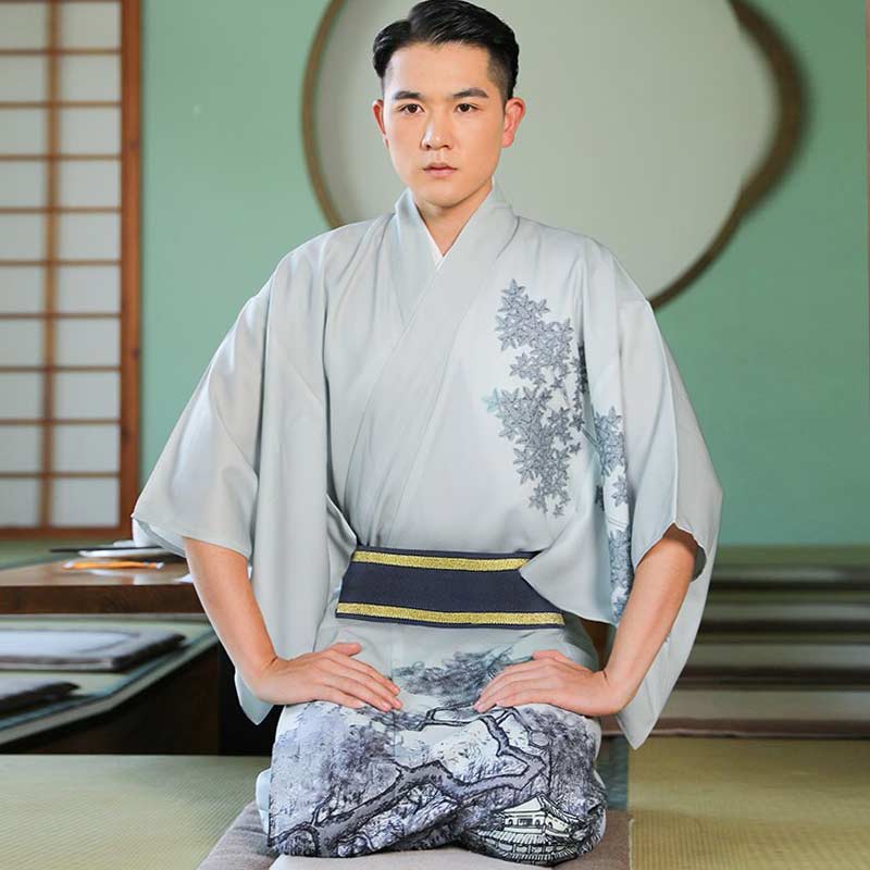 A man sitting on a traditional Japanese floor setting, wearing a blue and white formal kimono for men with a floral pattern.