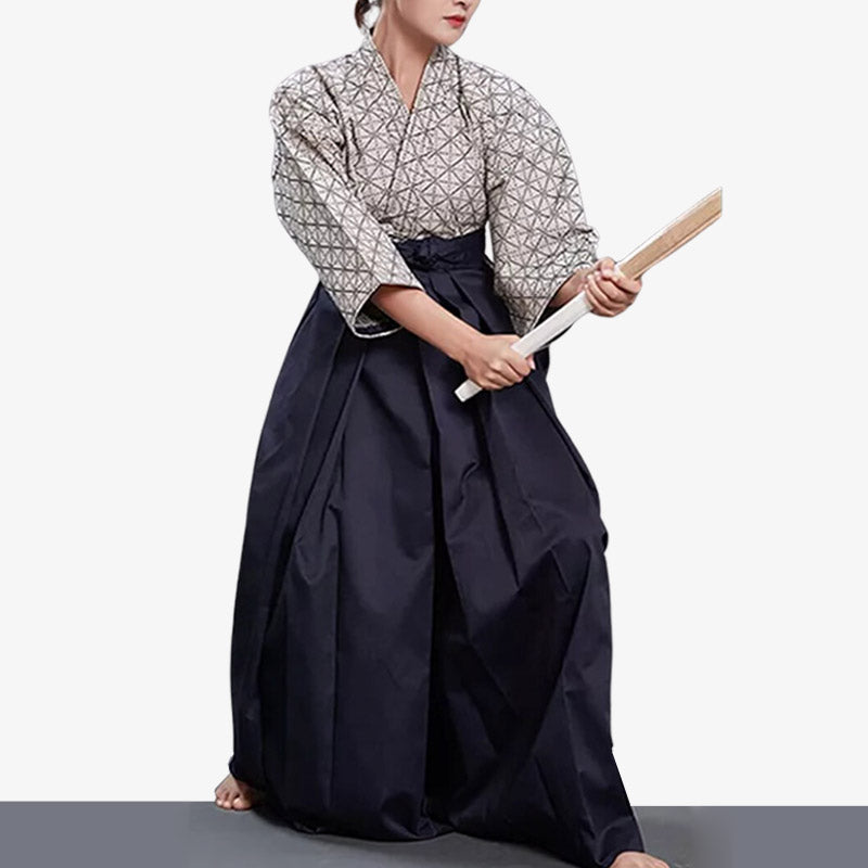 A person practicing Aikido wearing a traditional Hakama pants with a geometric pattern in navy blue and white colors, holding a bachi (strike punch) wooden katana.