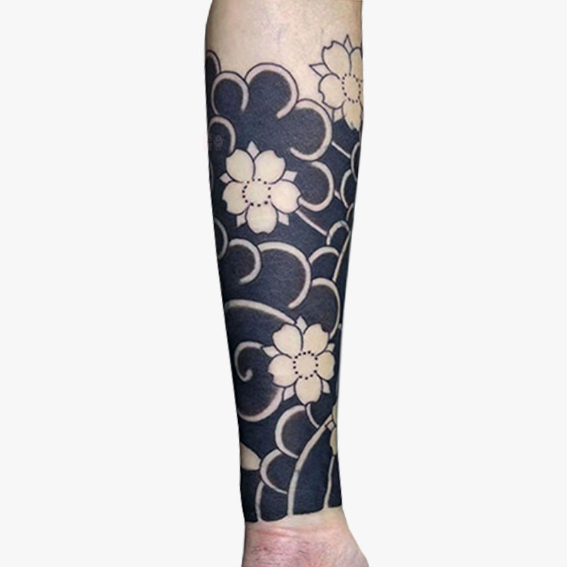 A temporary Japanese flower tattoo flash on a person's arm featuring a black and beige cherry blossom design, indicative of traditional Japanese Irezumi art.