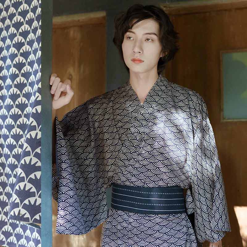 A Japanese man is standing. He is dressed in a Seigaiha Kimono pattern. Kimonot material is light cotton with a Japanese obi belt.