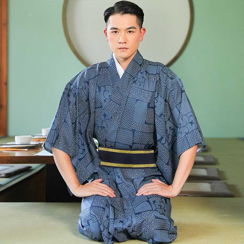 A man wearing a traditional Japanese men kimono with geometric blue patterns, paired with a belt with a gold-colored buckle, seated in a formal setting.
