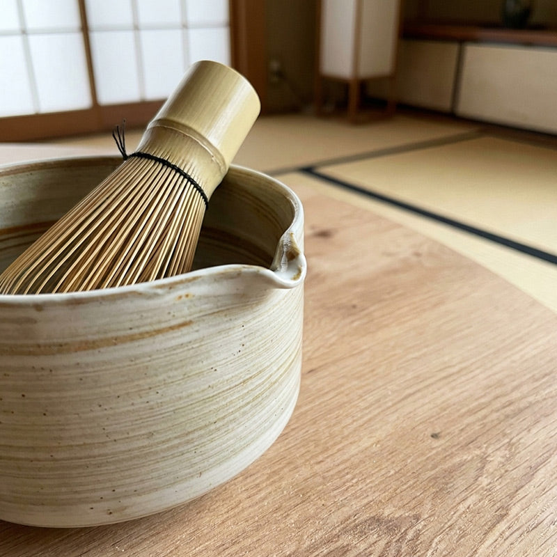 Bamboo whisk and ceramic bowl on a wooden floor with tatami mats in the background