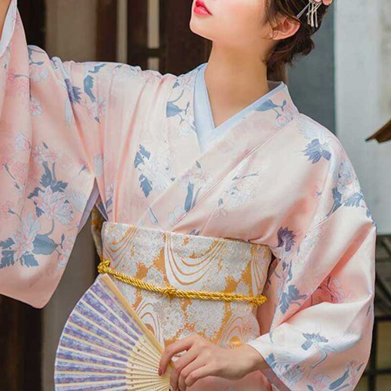 a japanese woman is dressed with a corset obi belt to hold her white kimono printed with japanese symbols
