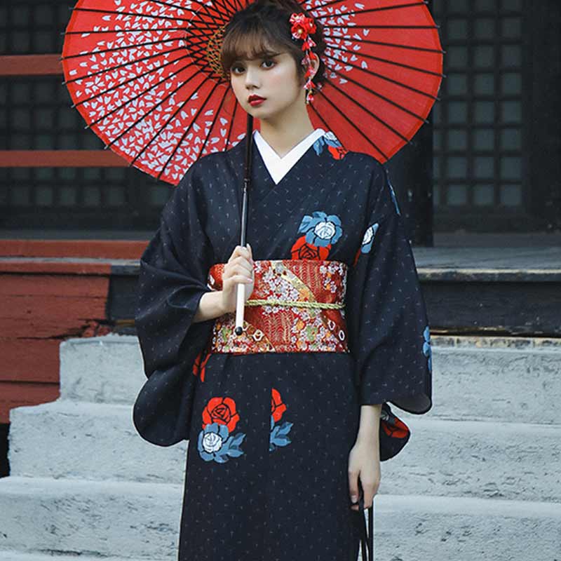 a japaonese women is dressed with cotton kimono with obi belt embroidered and red colored. The standing women hold a red umbrella in her hand