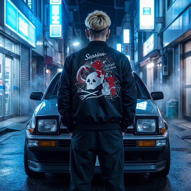 Person wearing a black etsy souvenir jacket with a graphic design standing in front of a vintage trueno car in a Japanese street