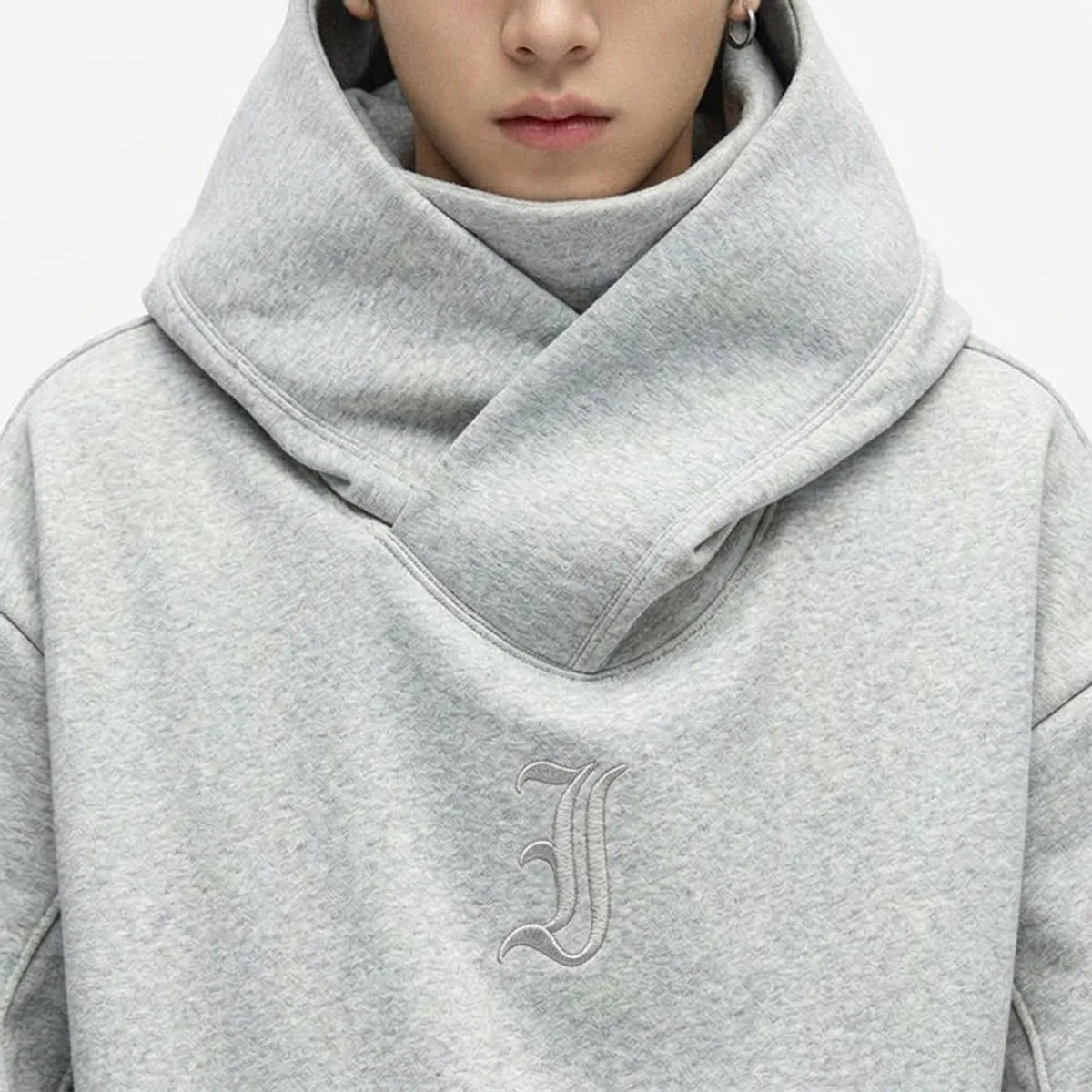 Close view of the crossed funnel neck of the hoodie and the small tone-on-tone gothic J embroidered on the chest