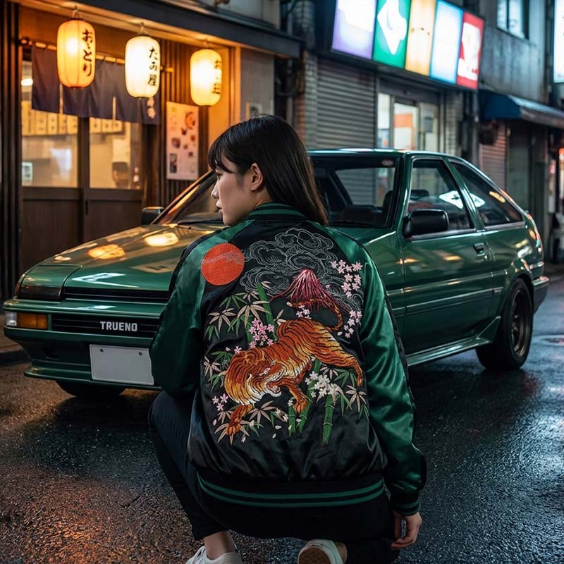 woman wearing a green sukajan jacket with a Tiger design in front of a green Trueno car in a Tokyo street