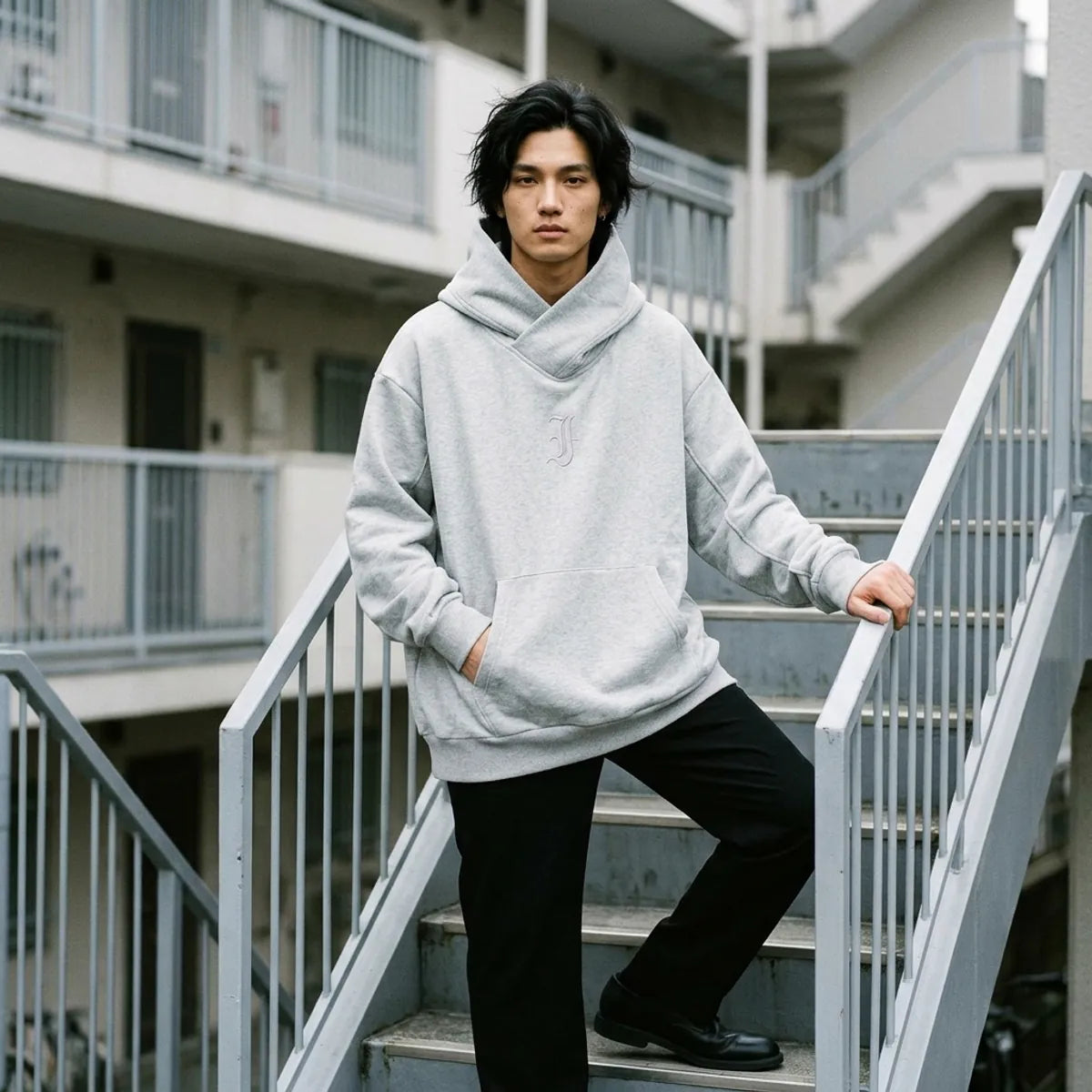 The heather grey hoodie for men worn standing on the concrete steps of a Tokyo apartment building