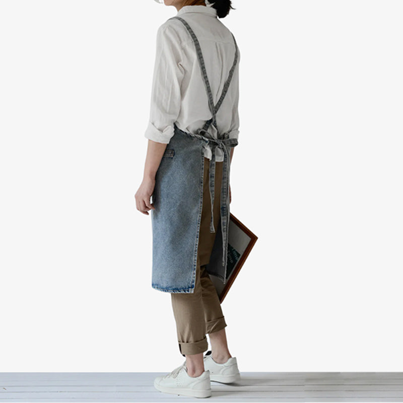 Japanese denim work apron in blue, designed with cross-back straps and a front pocket, offering durable protection and style for kitchen and workshop tasks.
