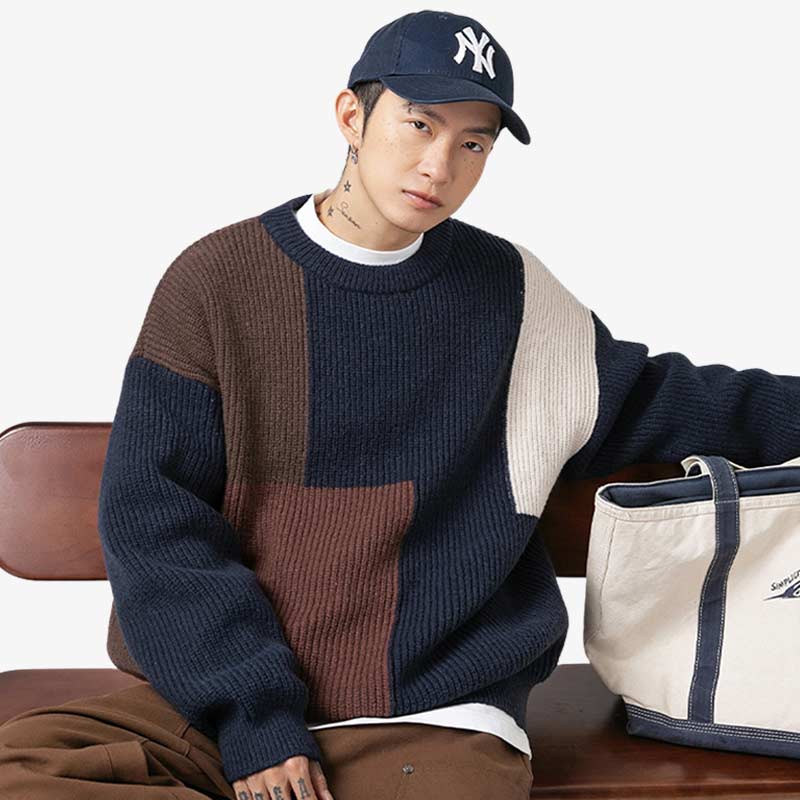 a man is sit on a chair. he is dressed with a japanese-oversize-sweater. Material of sweater is cashemire and color is navy. The man is also wearing a hat