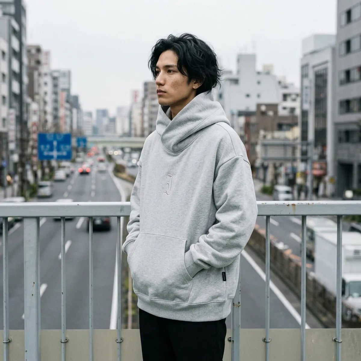 Japanese streetwear grey hoodie worn on a pedestrian bridge above a wide Tokyo avenue under an overcast sky