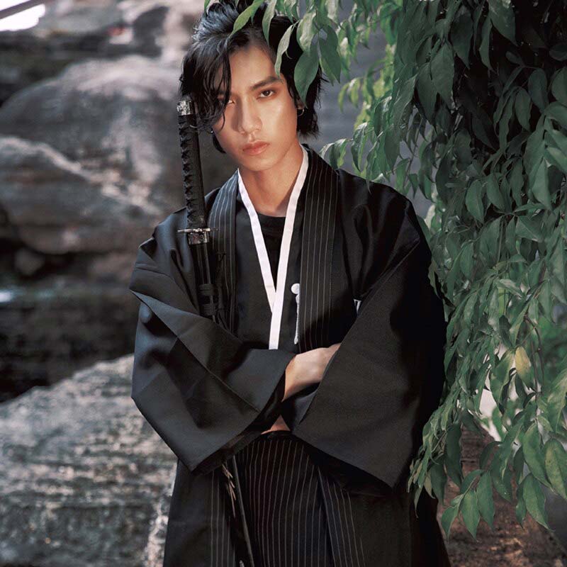 A Japanese man is dressed in a Kimono Men Traditional. Kimono fabric is cotton with black color.Japanese man's kimono, holding a kanzashi under his arm. It's a small katana