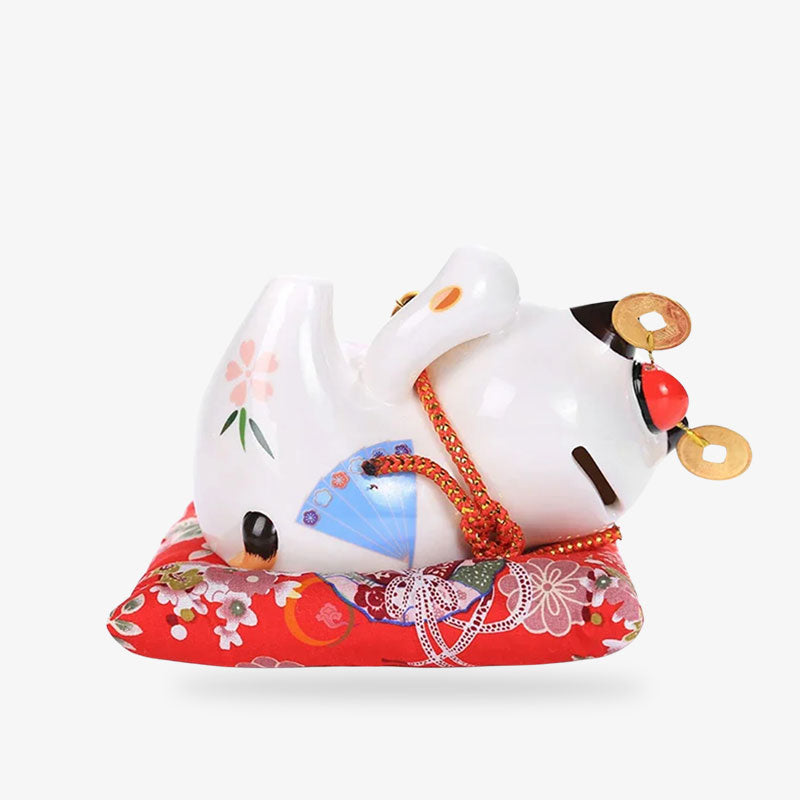 a Japanese ceramic maneki neko money bank statue is lying on a red cushion