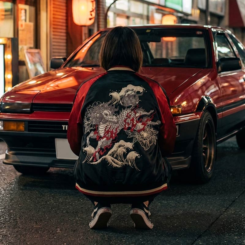 Person wearing a black and red Kirin sukajan jacket with a embroidered desing in front of a the famous Initial.D car on a Tokyo Street