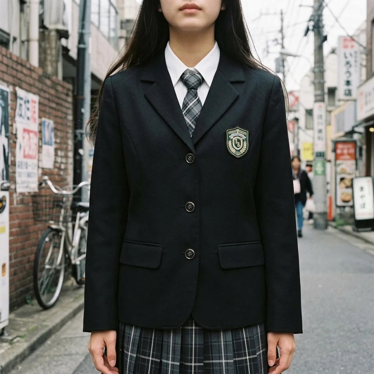 Close view of the black school blazer, the embroidered shield crest, the white collar and the plaid tie