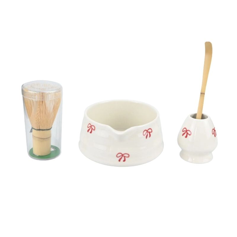 Set of Japanese tea-making tools including a glass cup, wooden whisk, and small container on a white background.