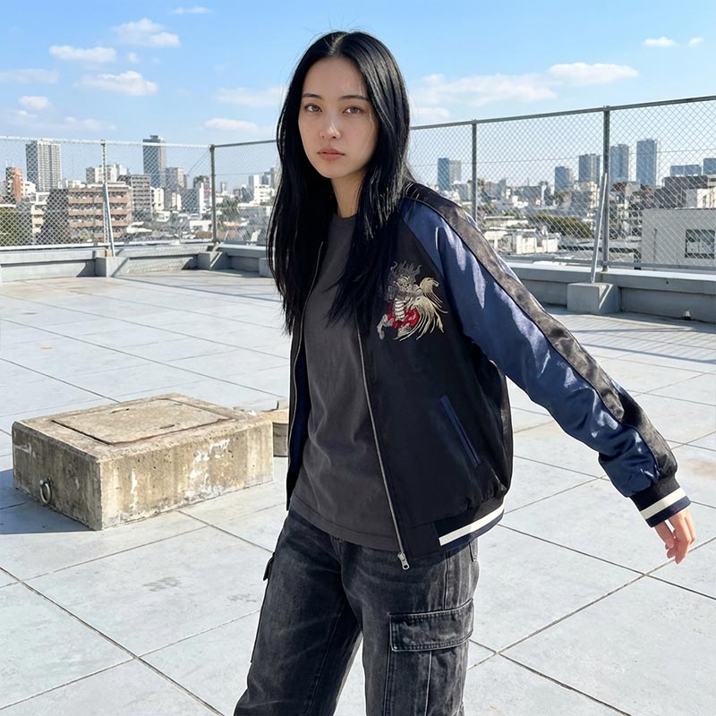 Person wearing a black and blue souvenir jackets Japan with a embroidered design on a rooftop with cityscape in the background