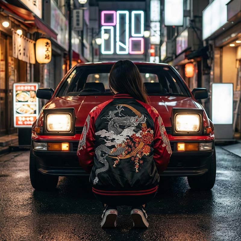 a woman wearing a stylish sukajan jacket with a dragon design sitting in front of a red car on a neon-lit street.