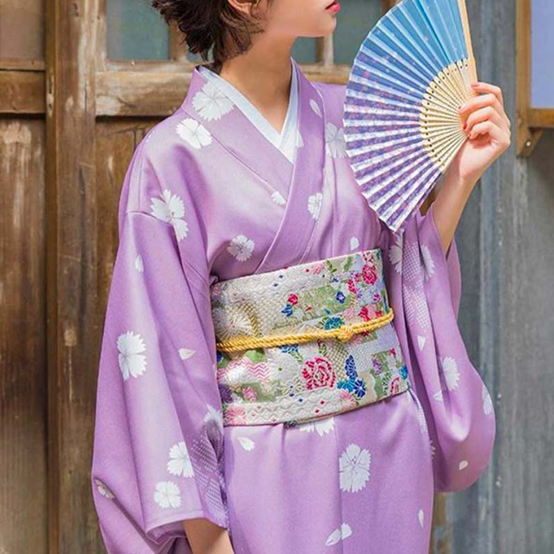 a standing woman is wearing a belt obi to tie her kimono traditional