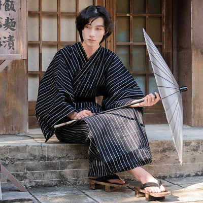 A Japanese man is dressed in a black kimono cosplay. He is holding a Japanese parasol and has put on geta wooden sandals.