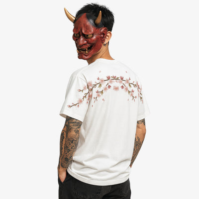 Person wearing a white embroidered shirt with cherry blossom design and a red devil mask on a white background