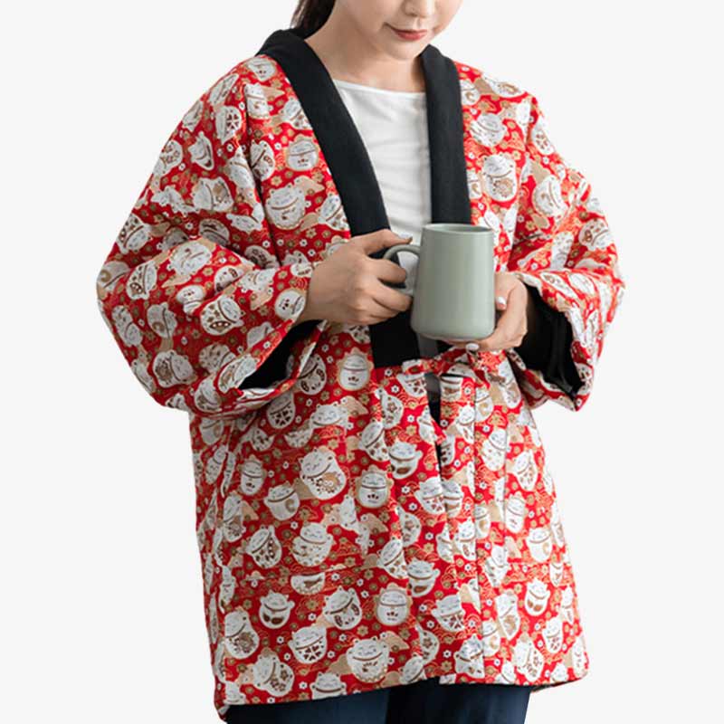 A woman wearing a red traditional Japanese Maneki Neko Hanten coat with white Japanese lucky cat patterns, holding a coffee mug.