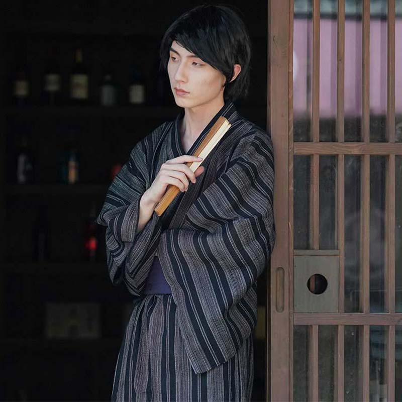 A japanese is Dressd in a Men tTraditional Kimono. Color kimono fabric is cotton grey with dark stripes. The man is holding a japanese fan in his hand