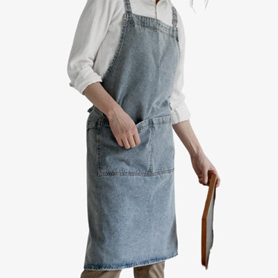Apron denim made from thick blue cotton fabric, featuring crossed shoulder straps and a practical front pocket for versatile use.
