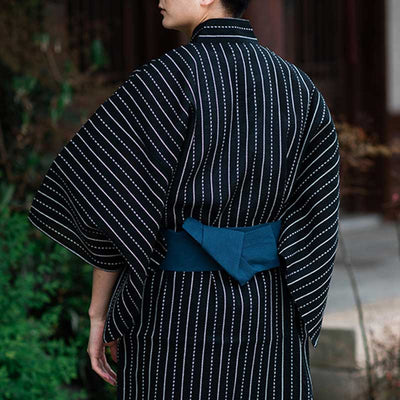 A Japanese man is wearing a black and white lace kimono cosplay. The Japanese yukata is fastened with an Obi belt.