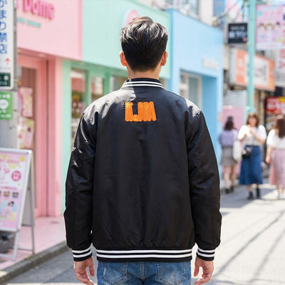 Person wearing a black bomber jacket male​ with 'LMA' on the back in an Harajuku street