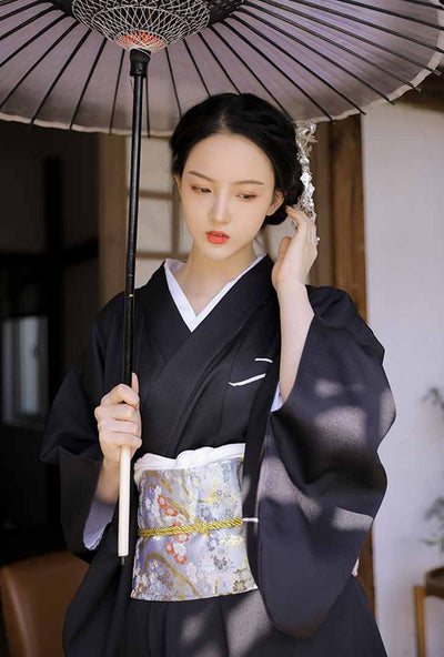 Black dress kimono adorned with japanese obi belt. The woman hold a japanese umbrella (wagasa) in her hand