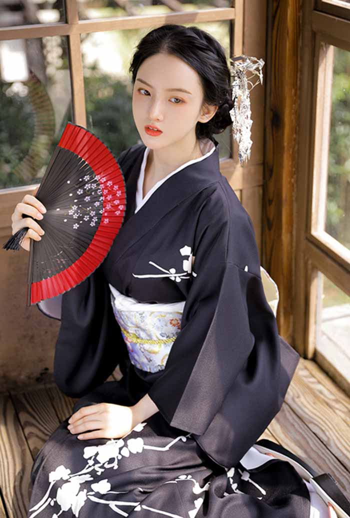 Black floral kimono dress with beautiful white flower designs. The woman holds elegantly a japanese fan