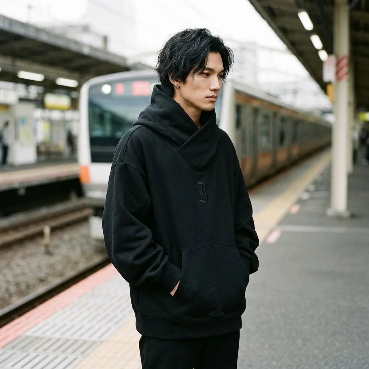 Black hoodie Japanese streetwear worn on an outdoor train platform in Tokyo under an overcast sky
