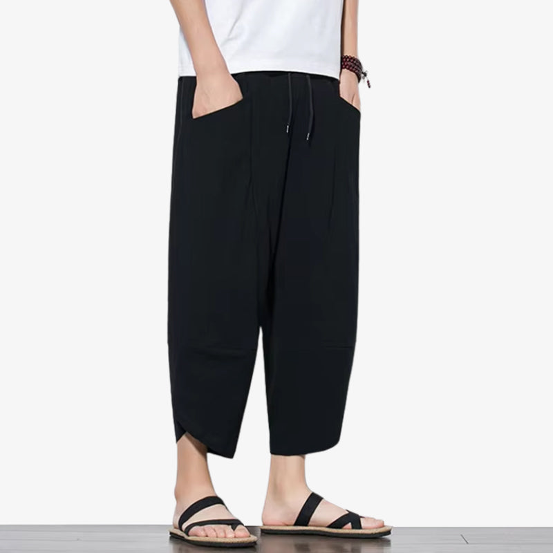 A man is dressed with a black japanese casual pants. he also wears sandals and a white zen t-shirt