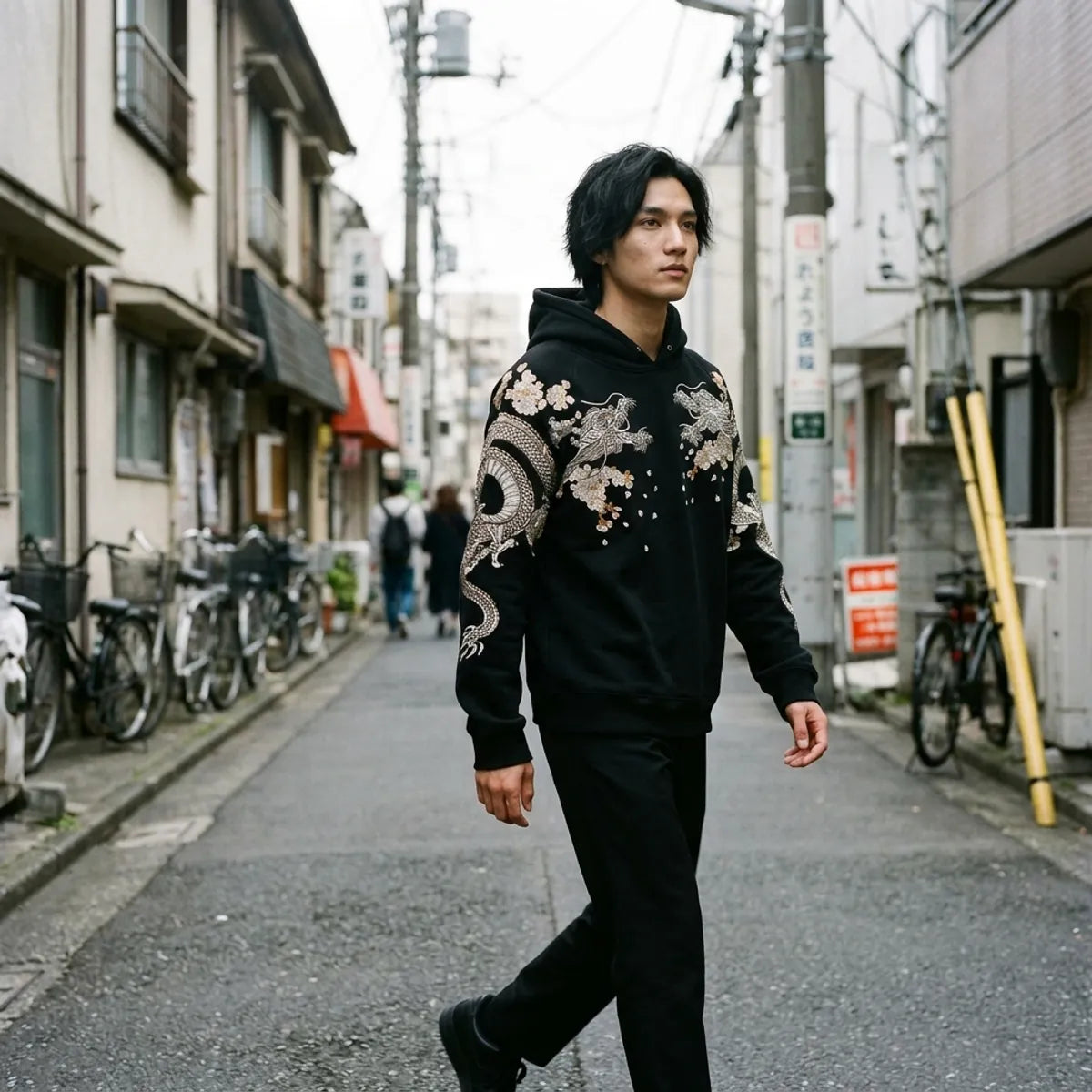Black Japanese hoodie streetwear look, the embroidered dragon sleeve caught mid step in Tokyo