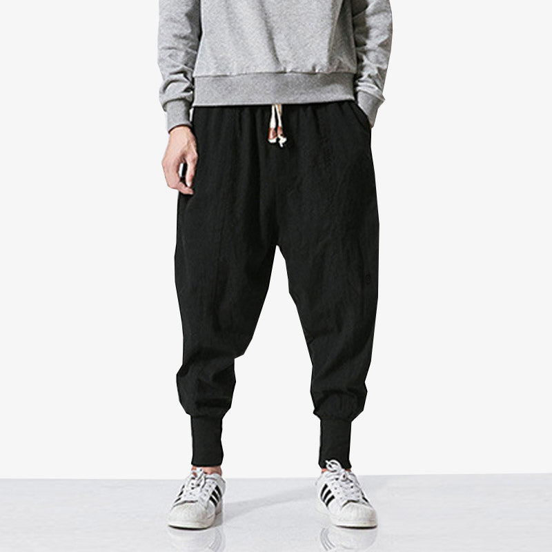 A Japanese man is wearing black pants streetwear with white trainers and a grey long-sleeved jumper.