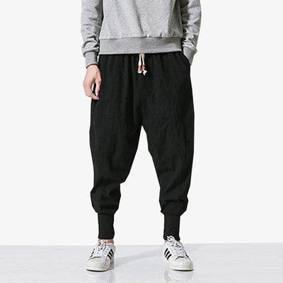 A Japanese man is wearing black pants streetwear with white trainers and a grey long-sleeved jumper.