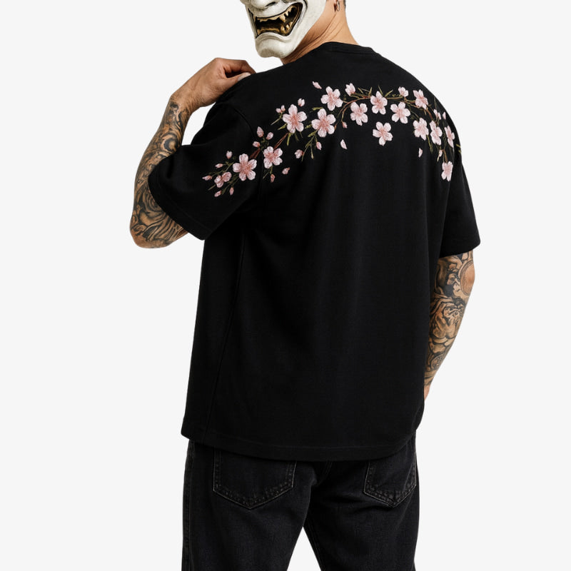 Person wearing a black sakura shirt with floral designs on the back, standing against a white background.