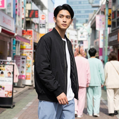 Man in a black Sukajan jacket standing on a busy Harajuku street with colorful signs and people in the background