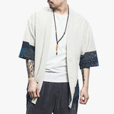 A man is standing wearing a short Cardigan Japanese-Clothe. This garment is a kimono jacket that can be worn over a t-shirt for a relaxed Japanese Zen style of dress. The haori jacket is white. It has a Zen Buddhist chaplet around the neck.