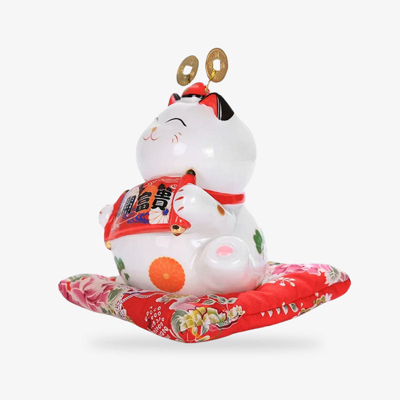 This lucky cat piggy bank japanese is a white ceramic maneki neko. It is a Japanese decorative object placed on a red cushion.
