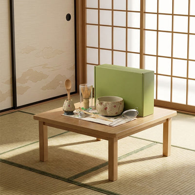 Wooden table with ceremonial matcha tea set and a green box in a traditional Japanese room.