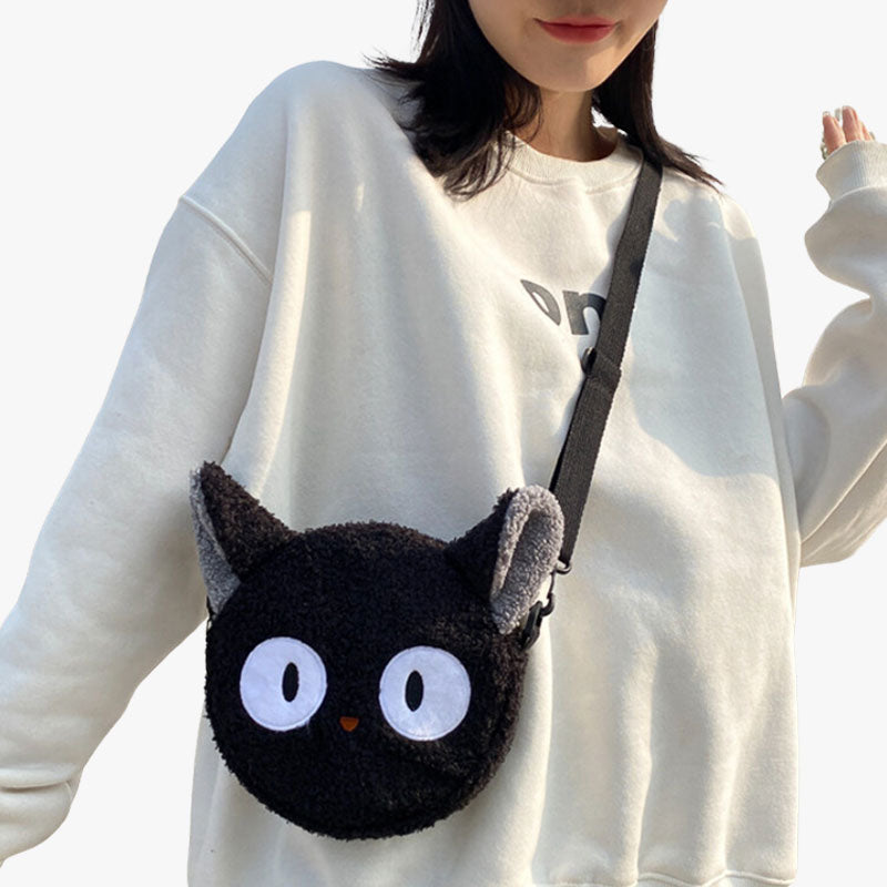 A woman is carrying a black cute kawaii bags in the shape of a black cat's head with big eyes. It's a shoulder bag made of soft material.