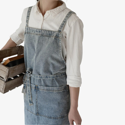 Denim apron in classic blue, with cross-back straps and a large front pocket, combining traditional Japanese workwear design with modern durability.