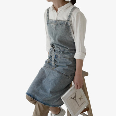 Denim Japanese apron featuring sturdy blue cotton, cross-back straps for comfort, and a convenient front pocket, ideal for cooking and craftwork.