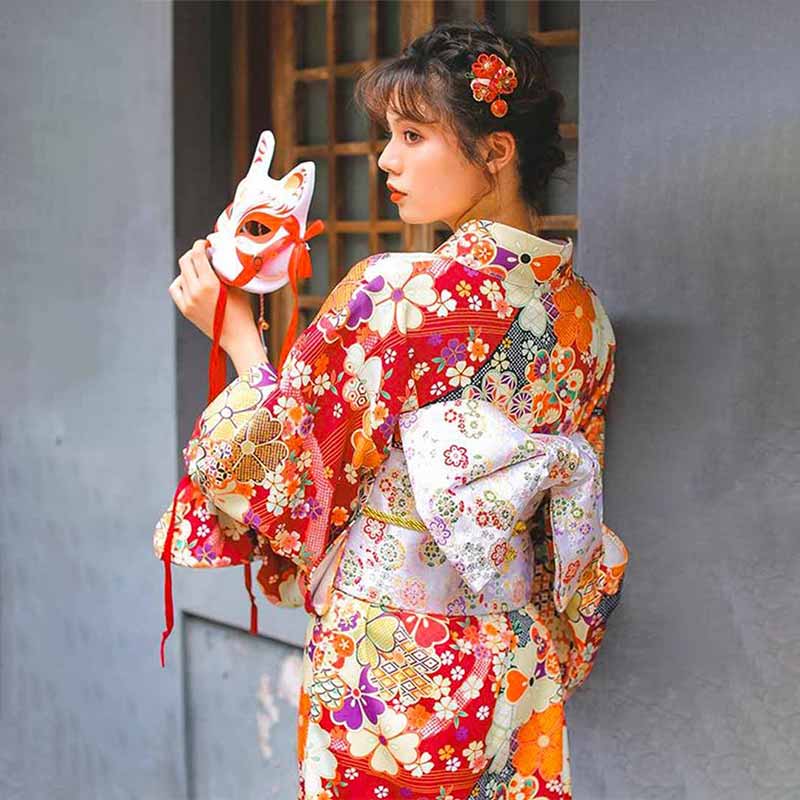 Geisha Japanese red kimono robe featuring beautiful sakura flower prints. The woman holds a Kitsune fox mask