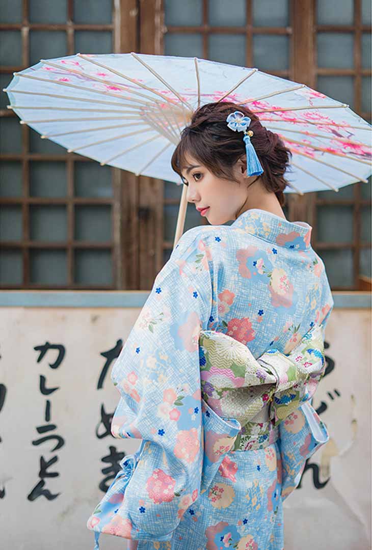 Geisha kimono robe adorned with Japanese flower prints. A woman stands gracefully, holding a traditional wagasa