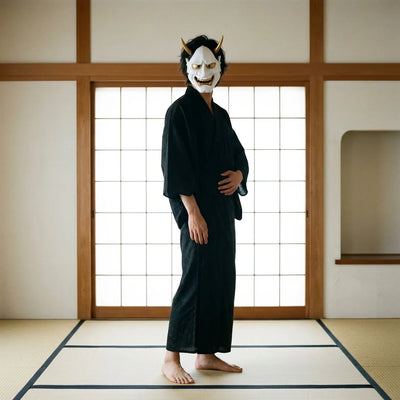The white Hannya mask standing upright on display, showing its curved gold horns and sharp painted teeth.