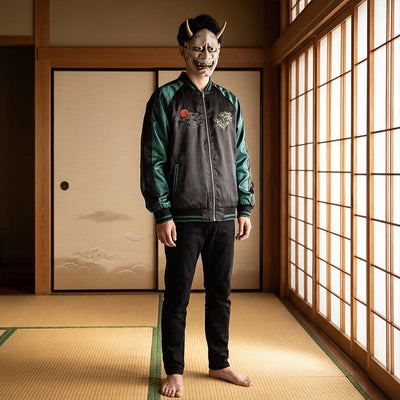 Person wearing a traditional Japanese mask and green souvenir jacket in a traditional washitsu room with wooden floors and sliding doors.